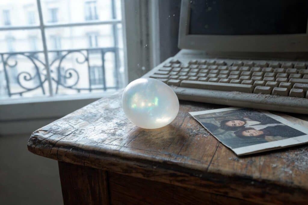 Œuf laiteux et mystérieux sur un bureau ancien, avec clavier poussiéreux et photo de famille, inspiré de Mœdium de Renée Zachariou.