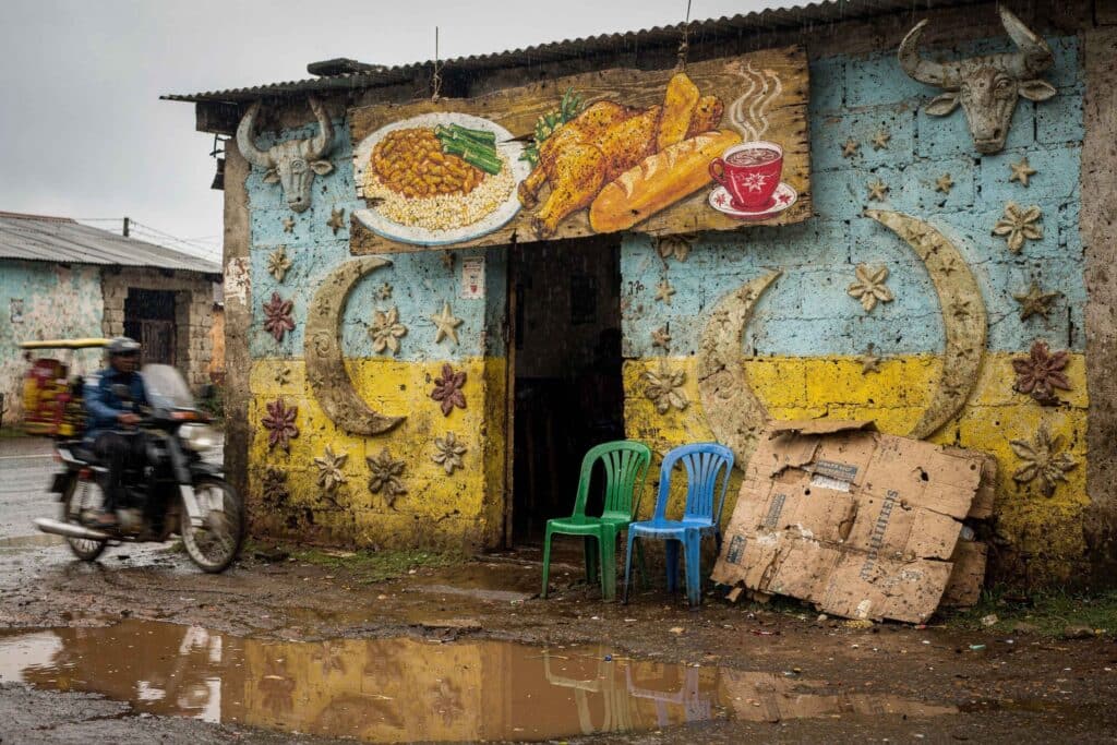 Façade peinte d'un petit restaurant de quartier sous la pluie, têtes de bœufs et croissants étoilés en relief, enseigne en contreplaqué représentant un plat, un poulet rôti et une tasse